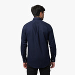 Back view of a man wearing a navy blue long-sleeved shirt and black pants against a white background