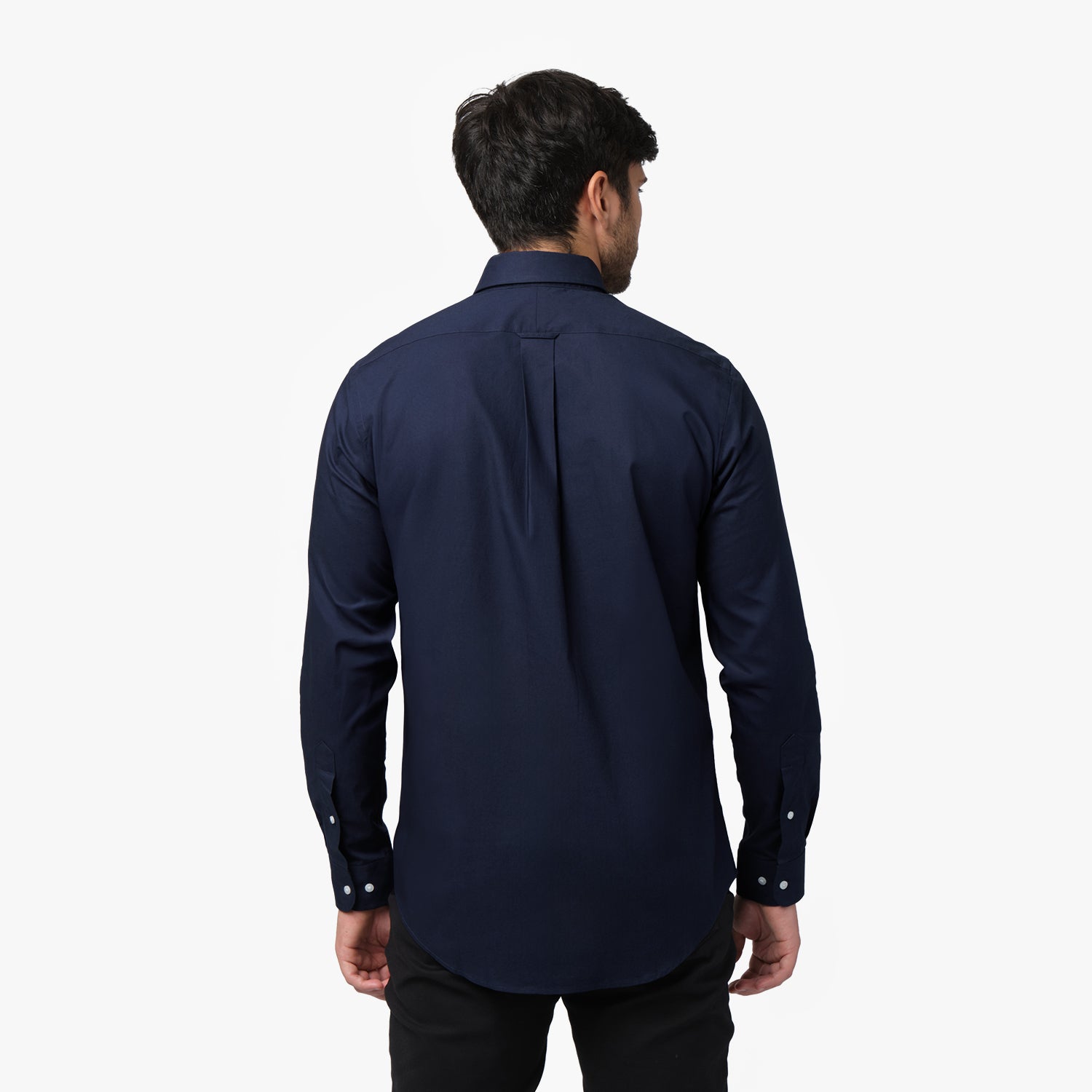 Back view of a man wearing a navy blue long-sleeved shirt and black pants against a white background
