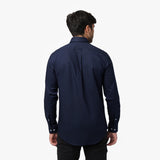 Back view of a man wearing a navy blue long-sleeved shirt and black pants against a white background