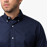 Close-up of a man wearing a navy blue long-sleeved button-down shirt, showing the collar, buttons, embroidered logo, and part of his face