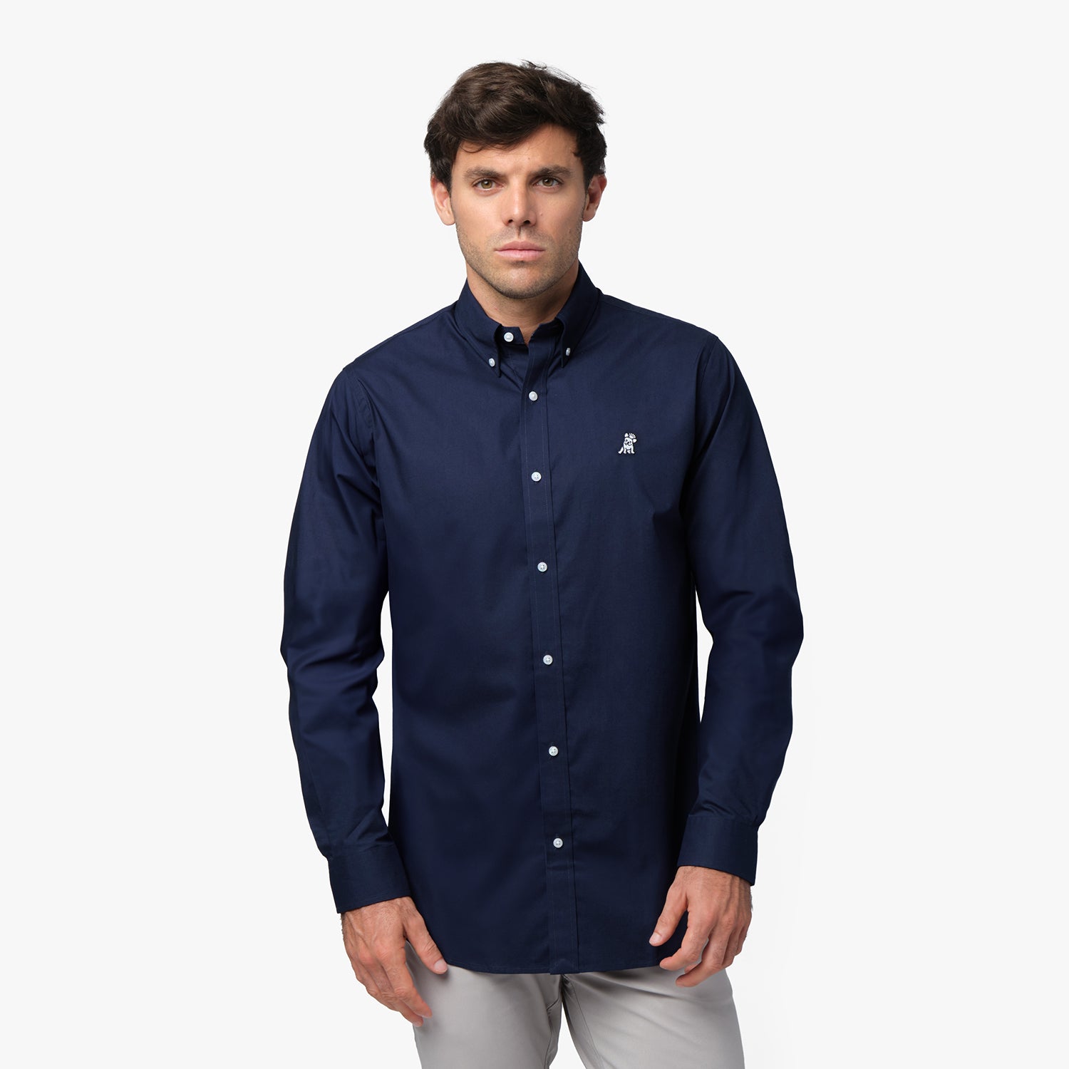 Full front view of a man wearing a navy blue long-sleeved button-down shirt with a white logo and light grey pants, standing against a white background