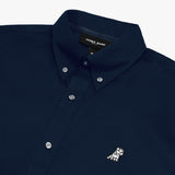 Close-up of a navy blue long-sleeved button-down shirt, showing the collar, buttons, the brand logo embroidered in white, and the neck label