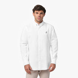 Front waist-up view of a male model wearing a white long-sleeve button-down oxford shirt with a small black embroidered logo on the left chest, paired with beige trousers