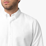 Close-up detail of the white oxford shirt collar and chest area on a male model, showing the button-down collar, buttons, fabric texture, and the small white embroidered dog logo on the left chest