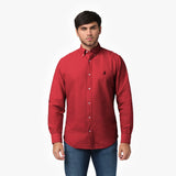 Front waist-up view of a male model wearing a red long-sleeve button-down oxford shirt with a small black embroidered logo on the left chest, paired with dark wash jeans