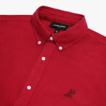 Close-up of the collar and upper chest area of a red button-down shirt. Features include a button-down collar, white buttons, a black "JAMES BARK" brand tag, and a tonal red embroidered dog logo on the left chest