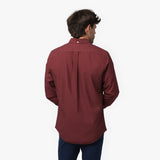 Back waist-up view of a male model wearing a burgundy long-sleeve oxford shirt with a back pleat, paired with navy trousers