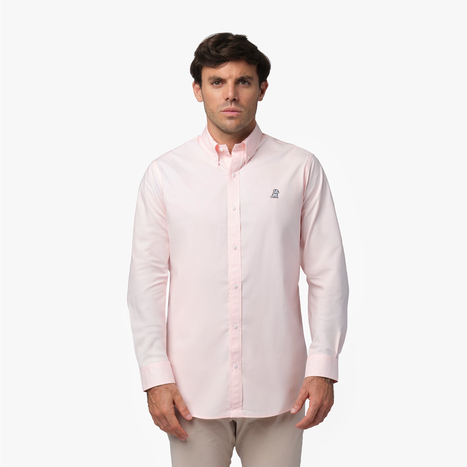 Full front view of a man wearing a pink long-sleeved button-down shirt with a small logo on the chest and khaki pants, standing against a white background