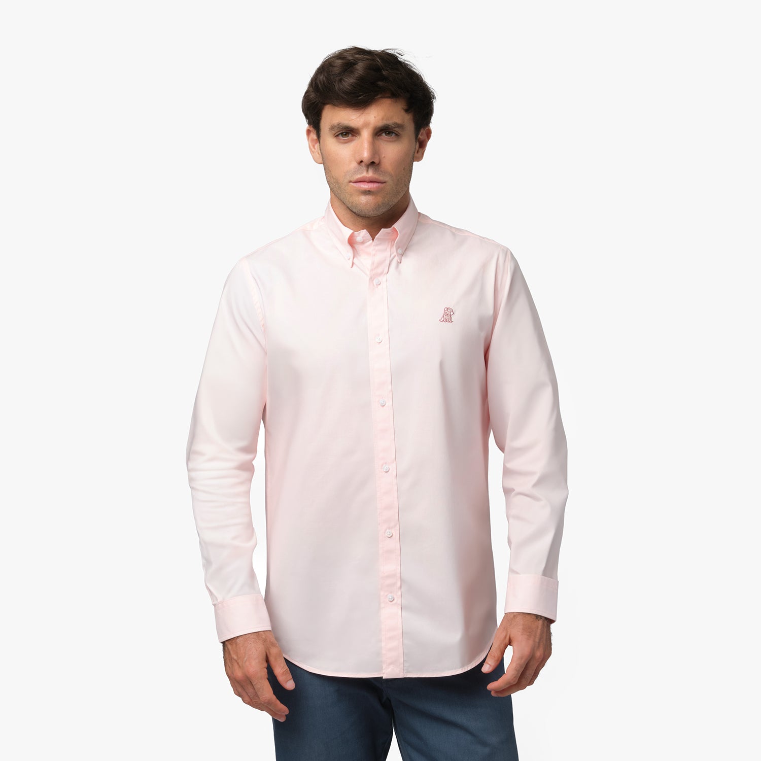 Full front view of a man wearing a pink long-sleeved button-down shirt with a pink logo and dark grey pants, standing against a white background