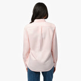 Back waist-up view of a female model wearing a light pink long-sleeve oxford shirt with a back pleat, paired with dark wash jeans