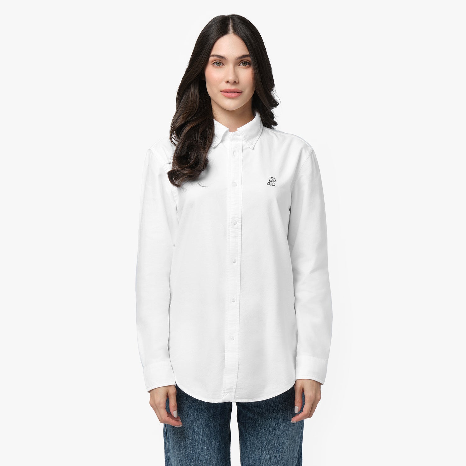Front waist-up view of a female model wearing a white long-sleeve button-down oxford shirt with a small black embroidered logo on the left chest, paired with dark wash jeans