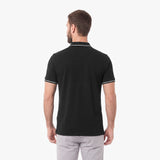 A man viewed from the back wearing a black polo shirt with white piping on the collar and sleeve cuffs