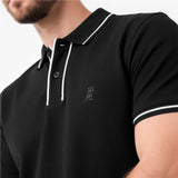 Close-up of a man wearing a black polo shirt with white contrast piping and a small dark embroidered dog logo on the chest.