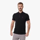 A man wearing a black short-sleeve polo shirt with red trim on the collar, placket, and sleeve cuffs, paired with light gray trousers