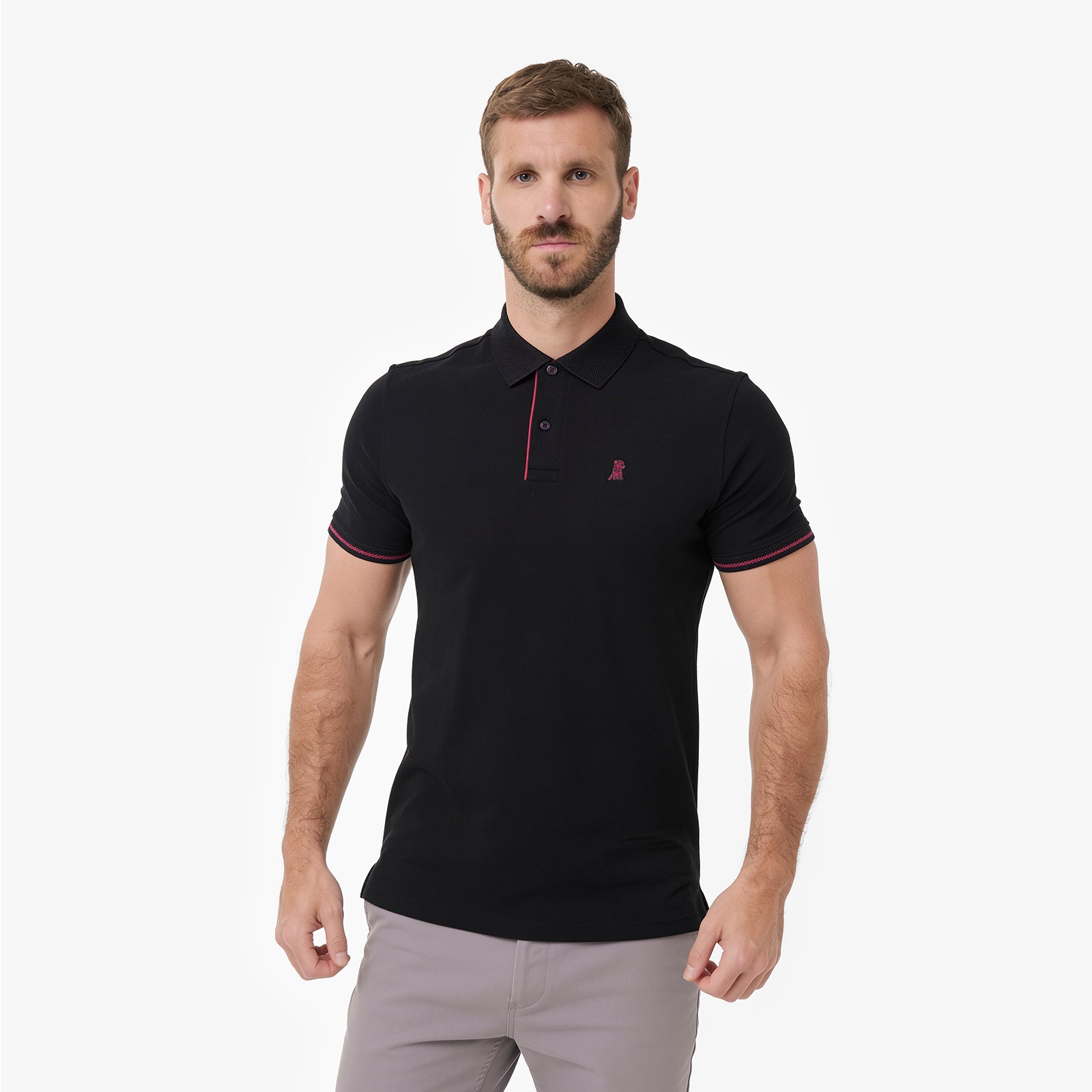 A man wearing a black short-sleeve polo shirt with red trim on the collar, placket, and sleeve cuffs, paired with light gray trousers