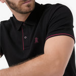 A close-up of a man wearing a black short-sleeve polo shirt with thin red piping along the collar and sleeve cuff, plus a small red embroidered logo on the chest.