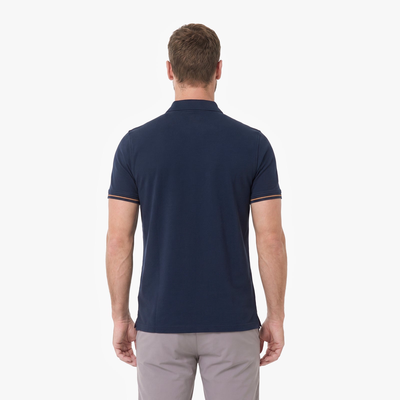 A man viewed from behind wearing a navy blue short-sleeve polo shirt with thin orange and white striped trim on the sleeve cuffs