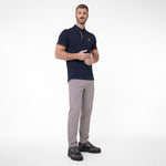 A man modeling a navy blue polo shirt with a small gold embroidered logo on the chest, paired with light gray trousers and black sneakers