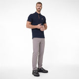 A man modeling a navy blue polo shirt with a small gold embroidered logo on the chest, paired with light gray trousers and black sneakers