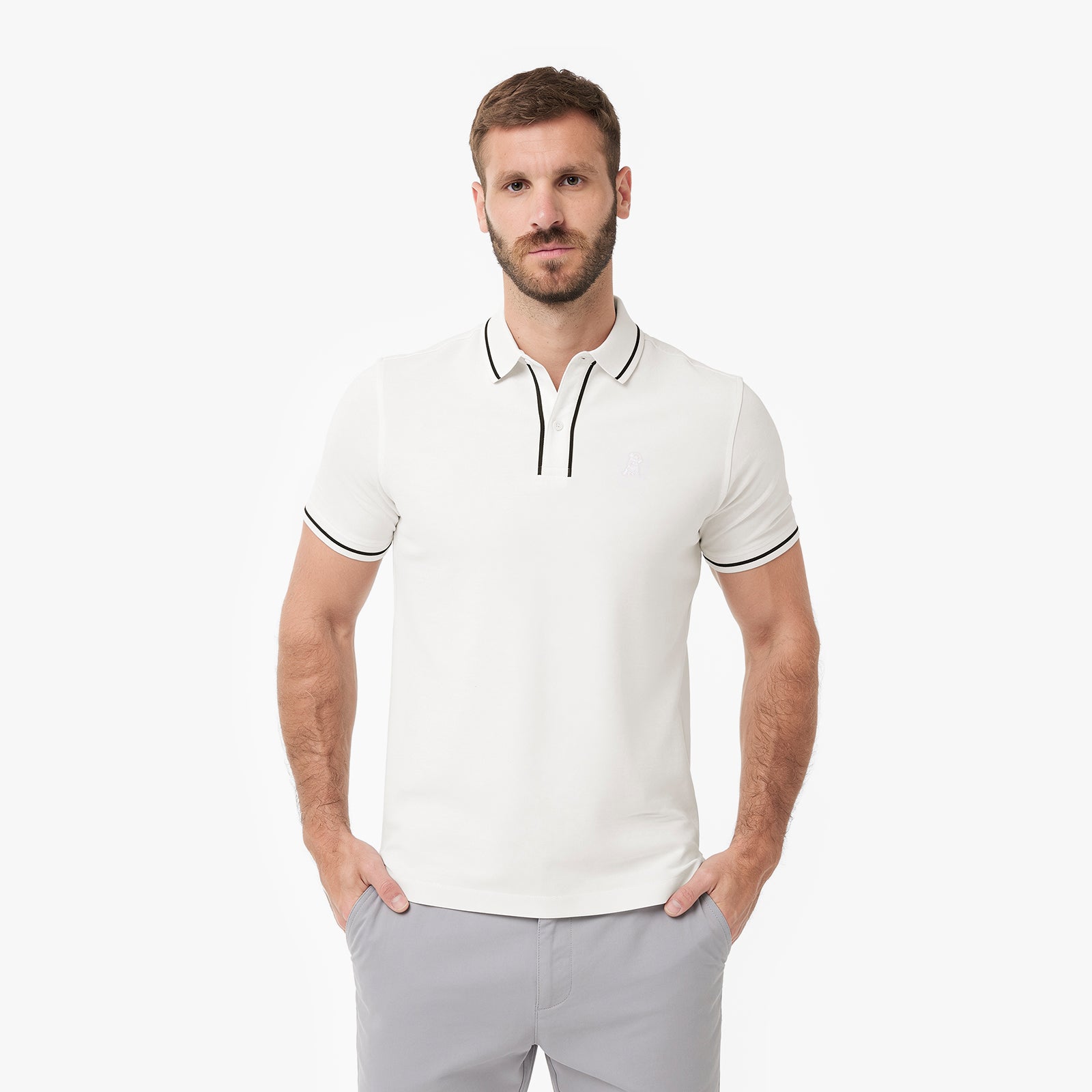 A man wearing a white polo shirt with black piping trim on the collar and sleeve cuffs, paired with light gray trousers