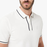 A close-up of a man wearing a white polo shirt with black piping trim on the collar and placket, featuring a small embroidered logo on the left chest.
