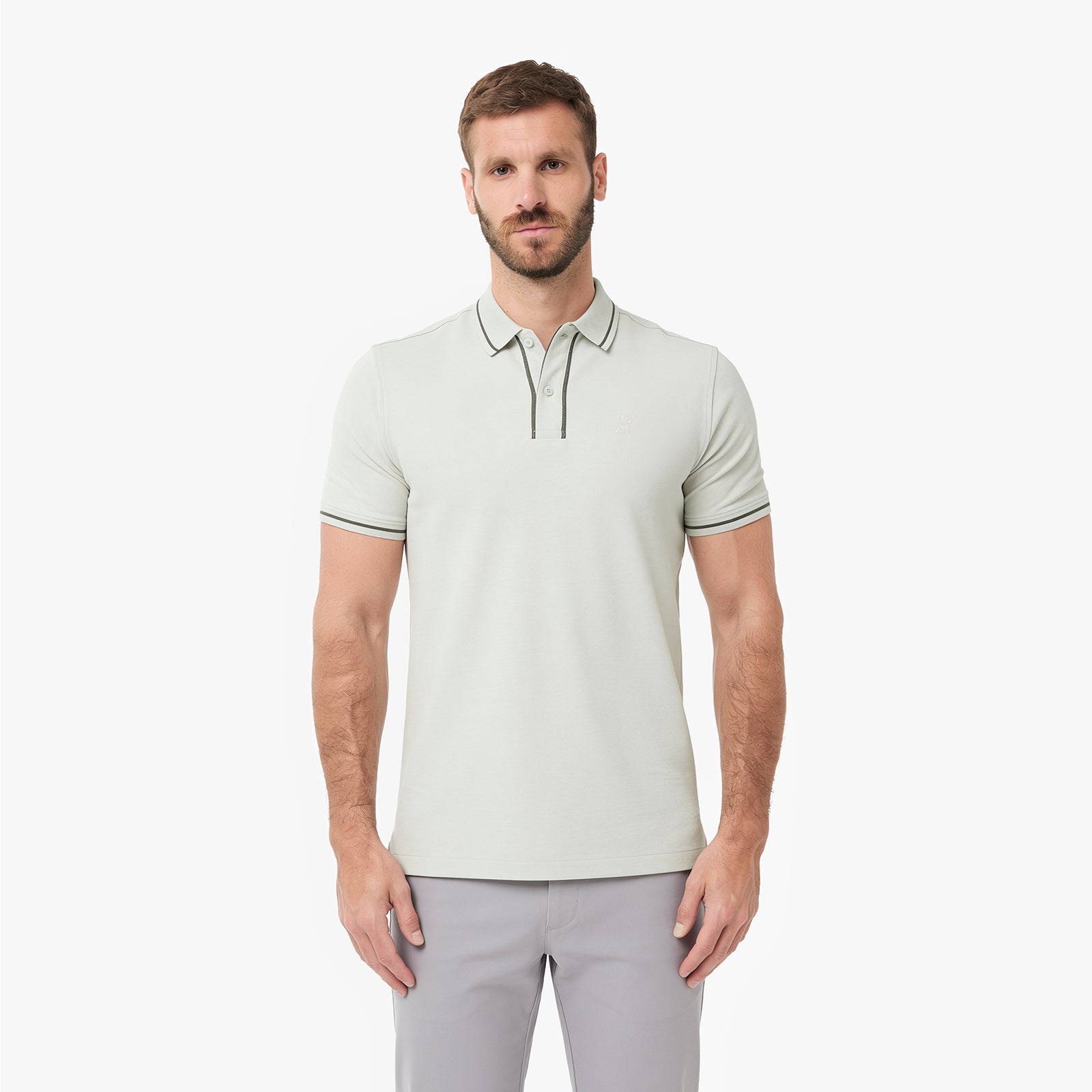 A man wearing a light sage green polo shirt with thin dark green stripe accents on the collar and sleeve cuffs, paired with light gray trousers