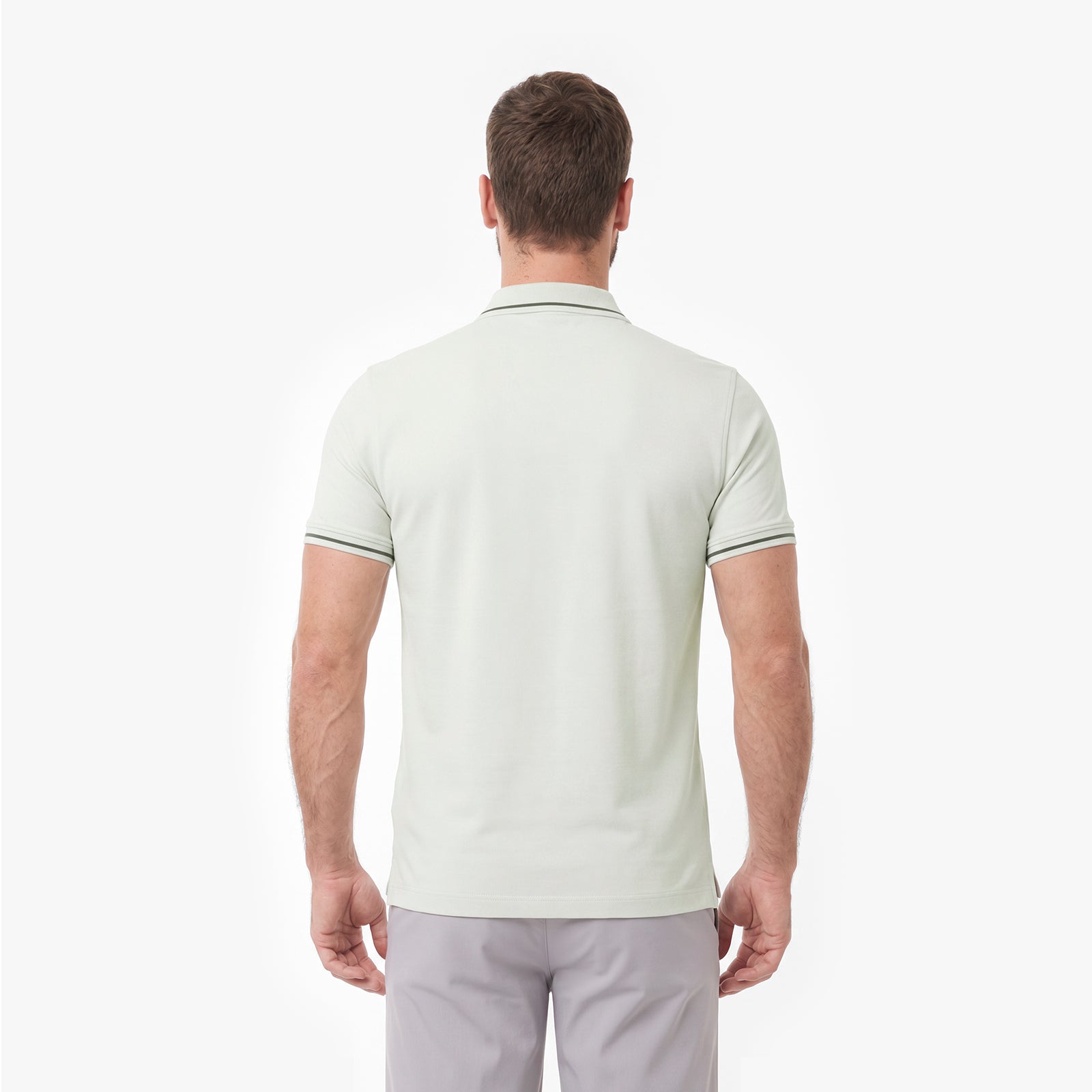 A man viewed from the back wearing a light sage green polo shirt with thin dark green stripe accents on the collar and sleeve cuffs, paired with light gray trousers