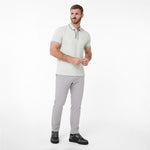 A man modeling a light sage green polo shirt with white and dark green trim, paired with light gray trousers and black shoes, against a white background.