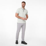 A man modeling a light sage green polo shirt with white and dark green trim, paired with light gray trousers and black shoes, against a white background.
