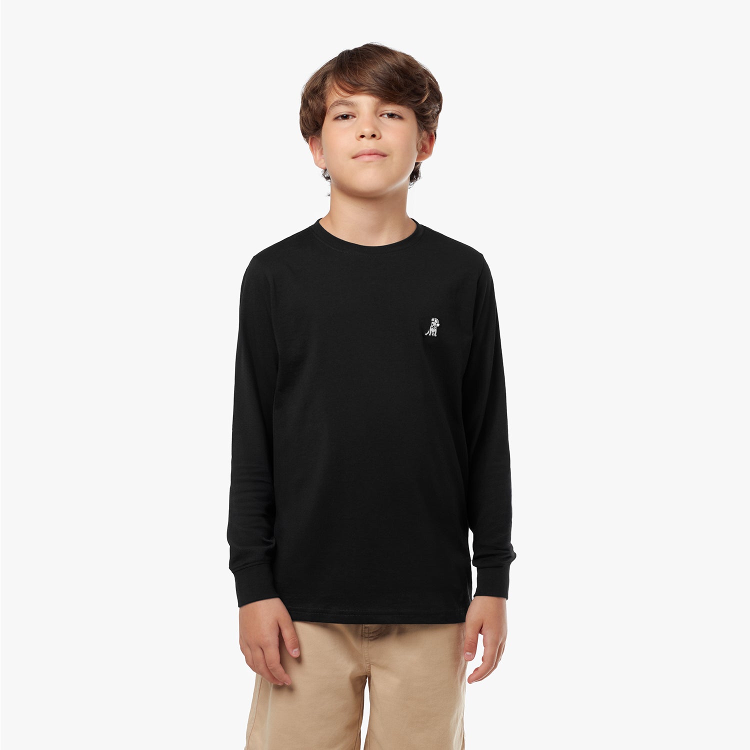  Young boy wearing a black long-sleeved t-shirt with a small logo and tan shorts, standing with hands in pockets and looking upwards
