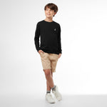 Young boy wearing a black long-sleeved t-shirt with a small logo and tan shorts, standing front view
