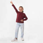 Full-body shot of the girl wearing the burgundy long-sleeve shirt paired with light blue pants, standing with her arm raised playfully.