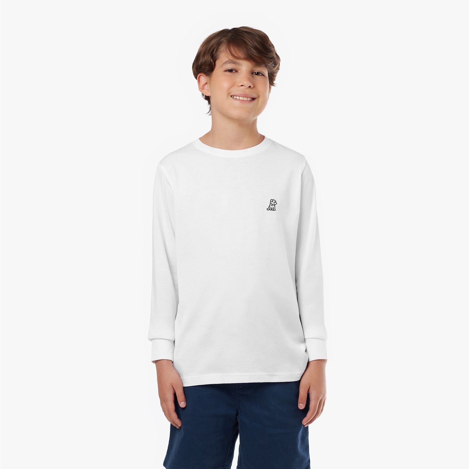 Young boy wearing a white long-sleeved t-shirt with a small dog logo and navy shorts, standing front view