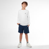 Full picture of a young boy wearing a white long-sleeved t-shirt with a small dog logo and navy shorts, standing front view