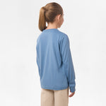 Side view of the girl wearing the light blue long-sleeve shirt, showing the plain back and relaxed fit.