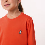 Close-up of the chest area of the orange shirt, featuring the small embroidered logo.