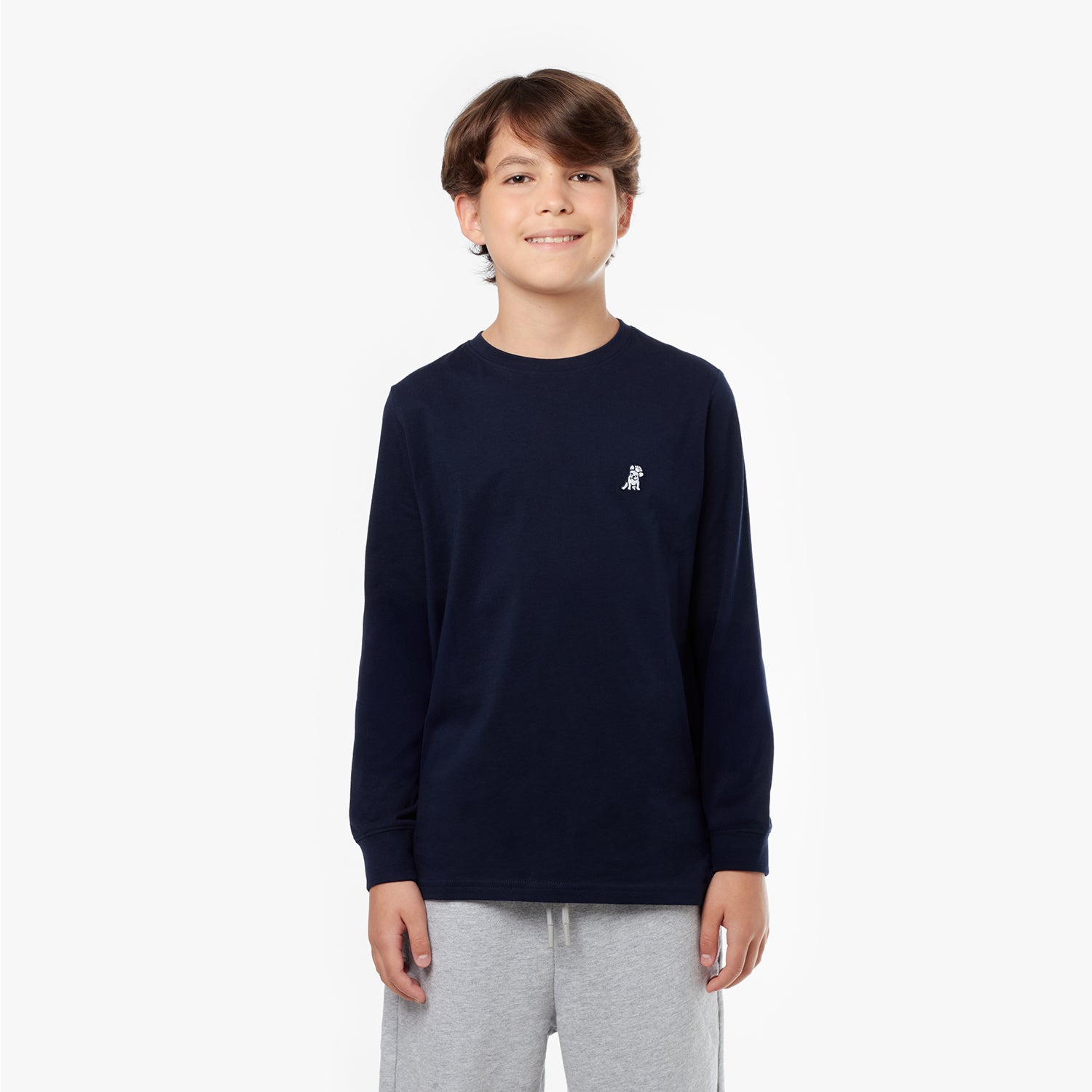 Young boy wearing a navy long-sleeved t-shirt with a small dog logo and tan shorts, standing with hands in pockets