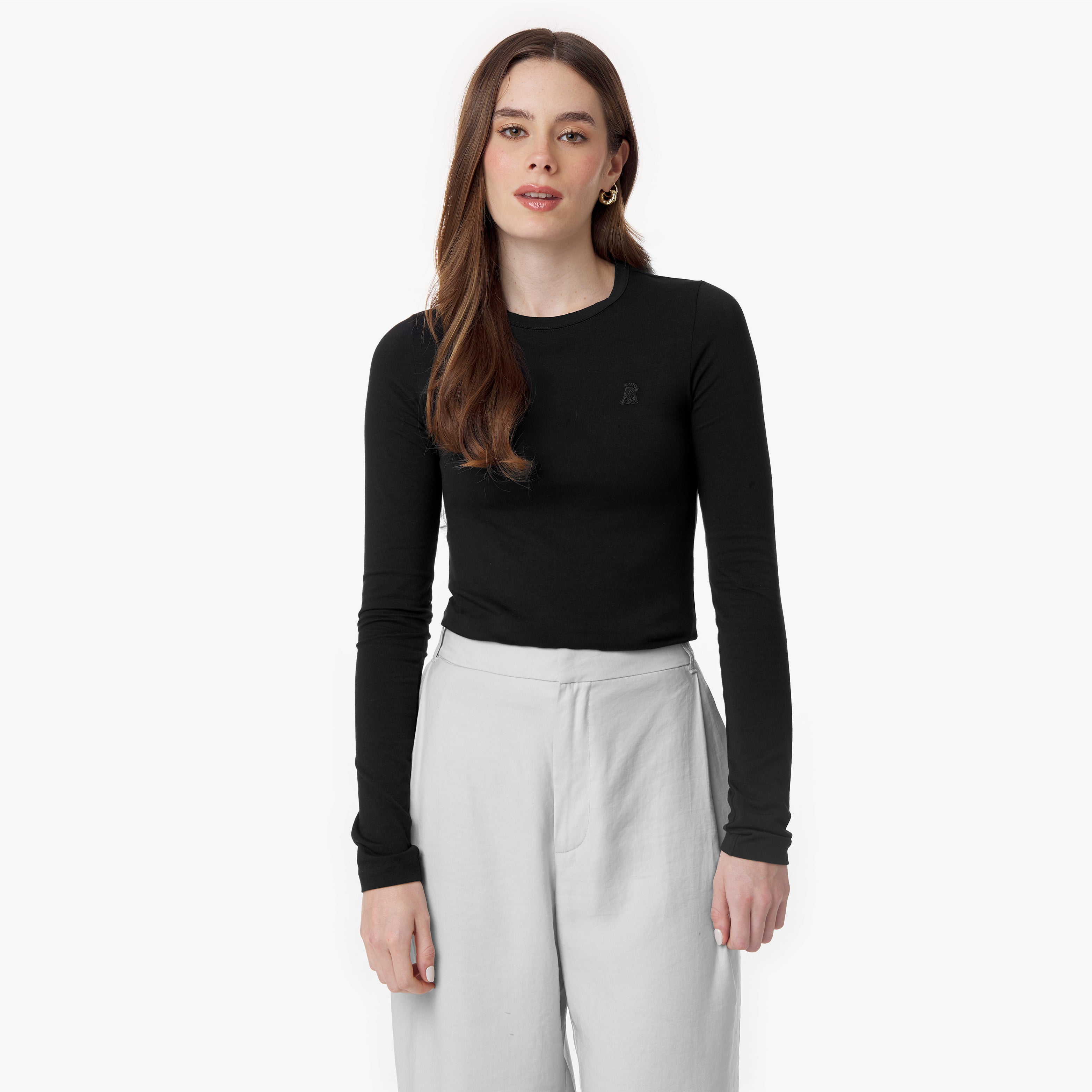 A straight-on view of the model standing in the black top and light gray trousers. Her neutral expression and the simplicity of the outfit emphasize a polished, minimalist aesthetic.