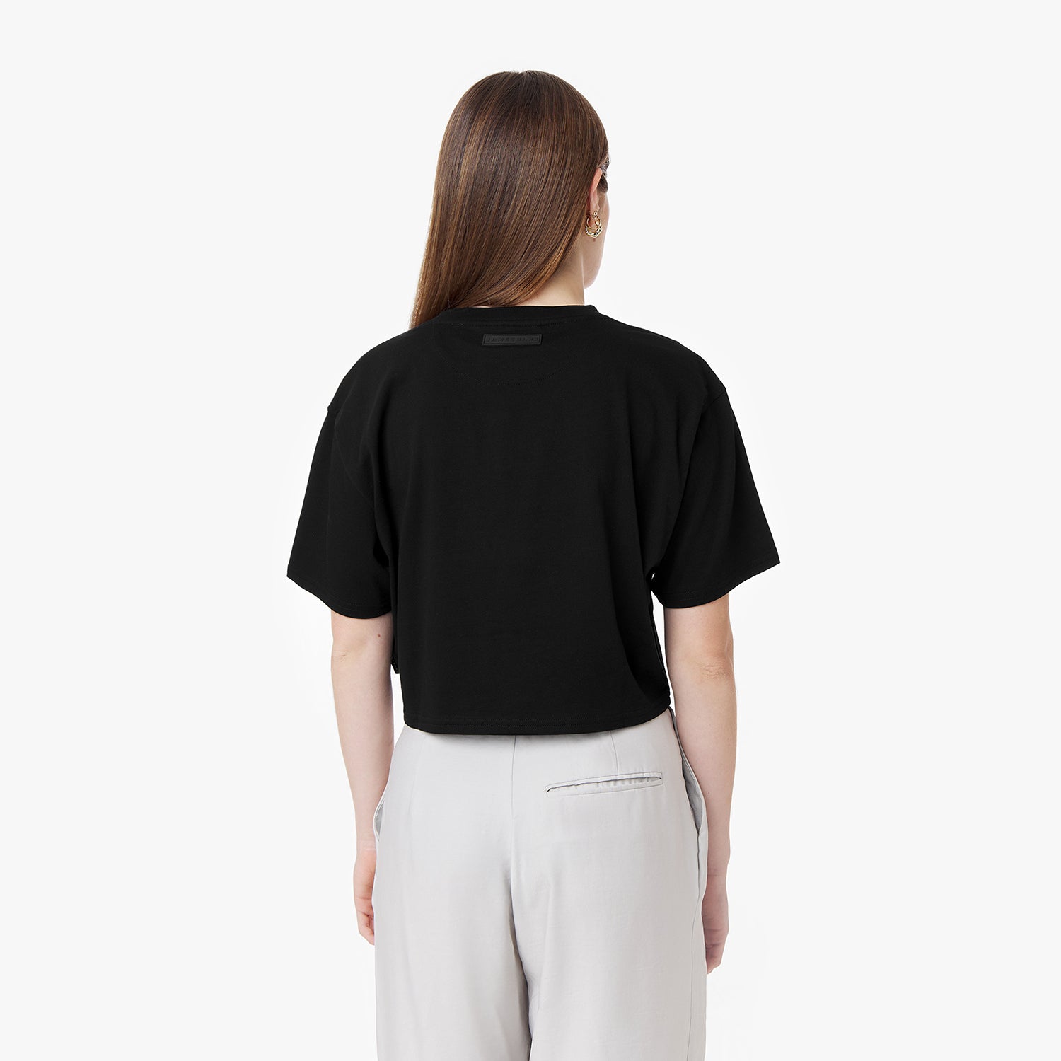 Rear view of the woman wearing the black cropped t-shirt and black joggers, hands on hips, showing the back of the shirt.