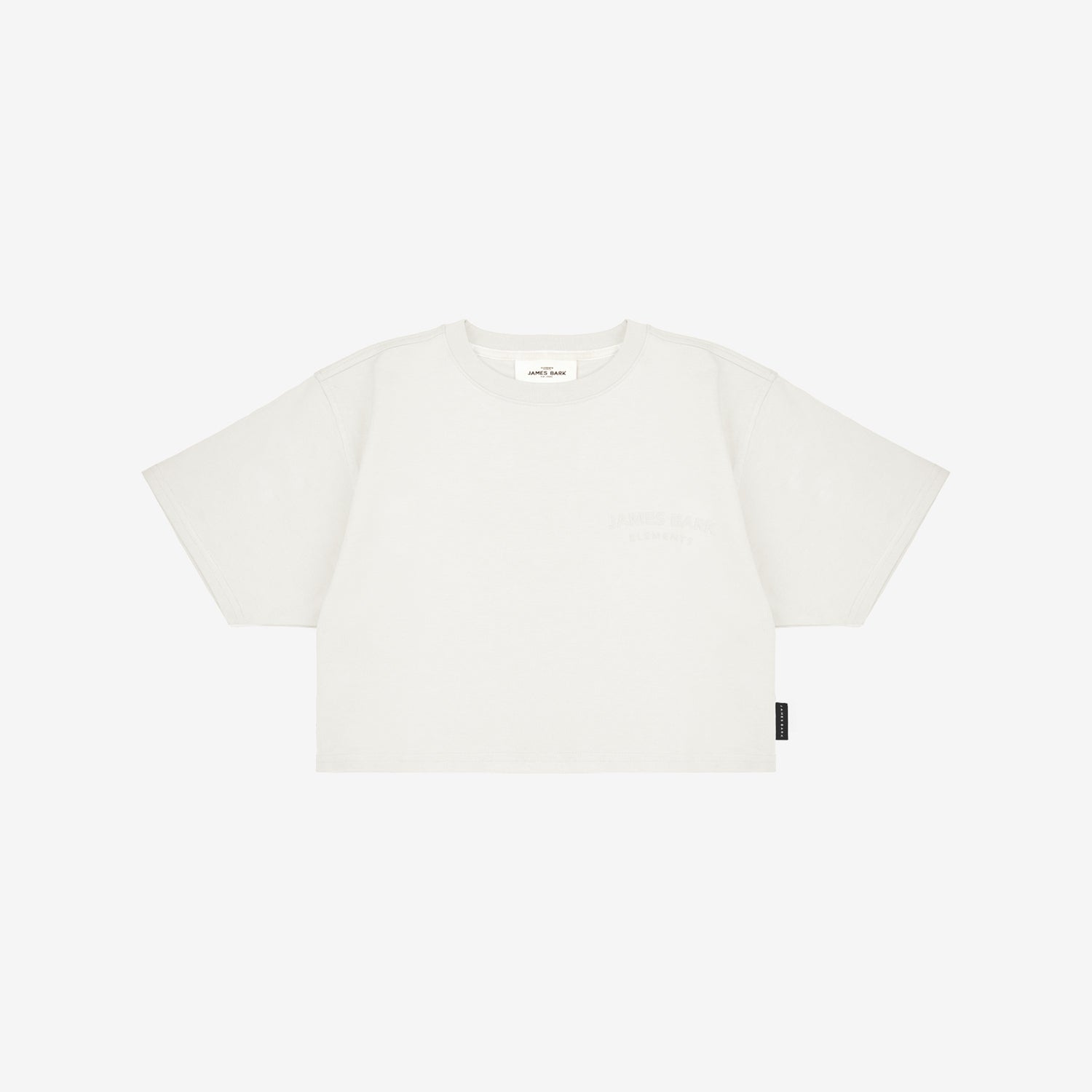 White boxy cropped t-shirt with short sleeves, featuring a minimalist design and a subtle logo on the chest. Black tag on the side. White background