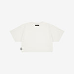 Back view of a white boxy cropped t-shirt with short sleeves. Features a minimalist design with a small black rectangular label near the neckline and a black tag on the side. White background