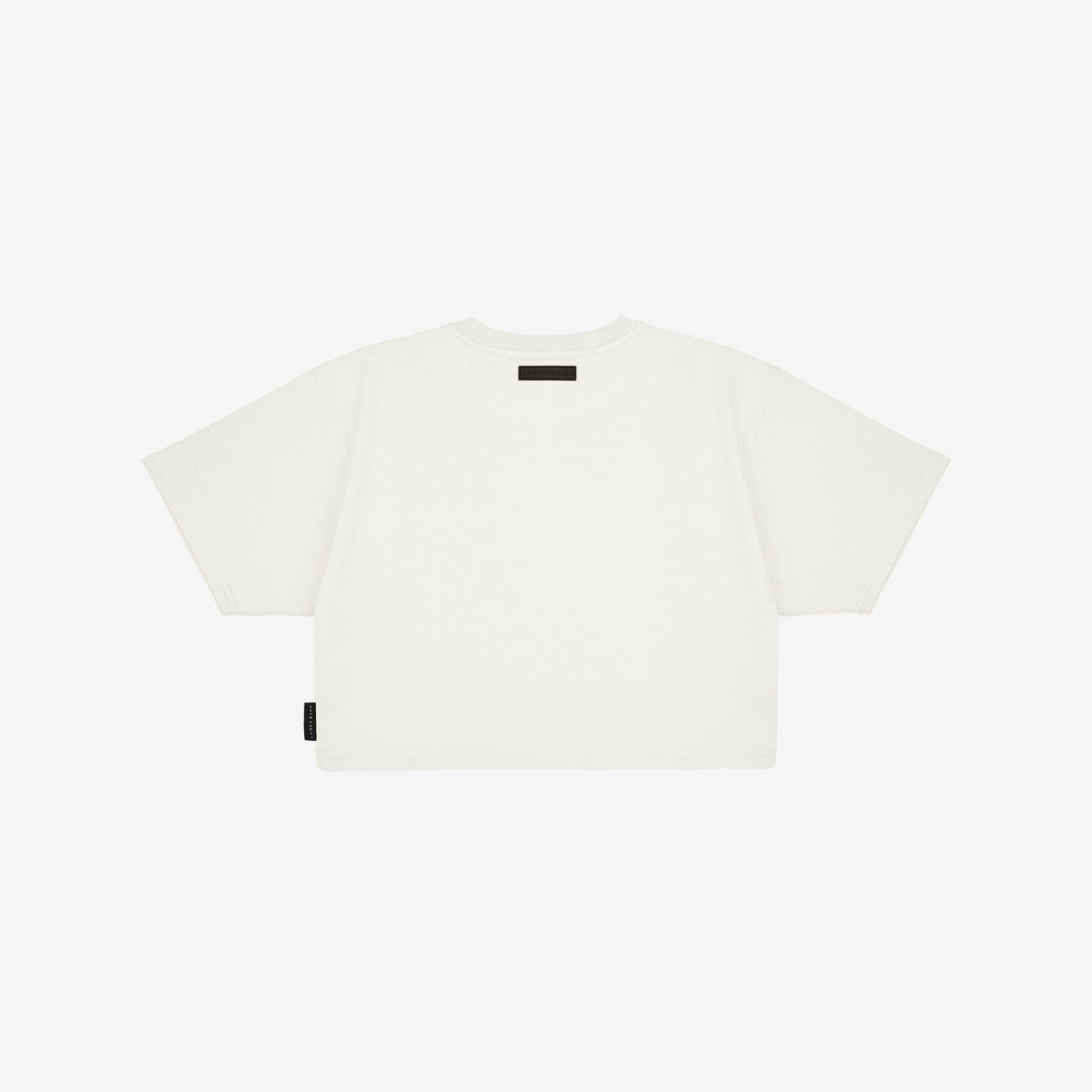 Back view of a white boxy cropped t-shirt with short sleeves. Features a minimalist design with a small black rectangular label near the neckline and a black tag on the side. White background