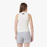 A female model with long brown hair is seen from the back wearing a fitted, ribbed white tank top with a high round neckline and a small black label at the upper back. She is also wearing light gray drawstring shorts. The background is plain white.