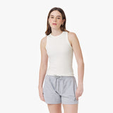 A female model with fair skin and shoulder-length brown hair wears a fitted, sleeveless, ribbed white tank top with a high round neckline. She pairs it with light gray drawstring shorts that have an embroidered small dog logo on the left leg. She accessorizes with gold hoop earrings and has a neutral expression with a soft gaze. The background is plain white.