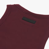 Close-up of the back of a burgundy ribbed tank top, highlighting a black rectangular 'JAMES BARK' label near the neckline. The fabric has a textured ribbed pattern with reinforced stitching along the edges. White background