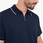 A close-up of a man wearing a navy blue polo shirt with a half-zip collar and white contrast piping on the collar and sleeve cuffs.