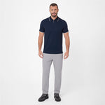 A man modeling a short-sleeve polo shirt in navy blue with white trim on the collar and sleeve cuffs, paired with light gray trousers and black sneakers