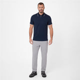 A man modeling a short-sleeve polo shirt in navy blue with white trim on the collar and sleeve cuffs, paired with light gray trousers and black sneakers
