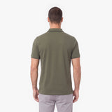 A man viewed from the back wearing an olive green short-sleeve polo shirt and light gray trousers