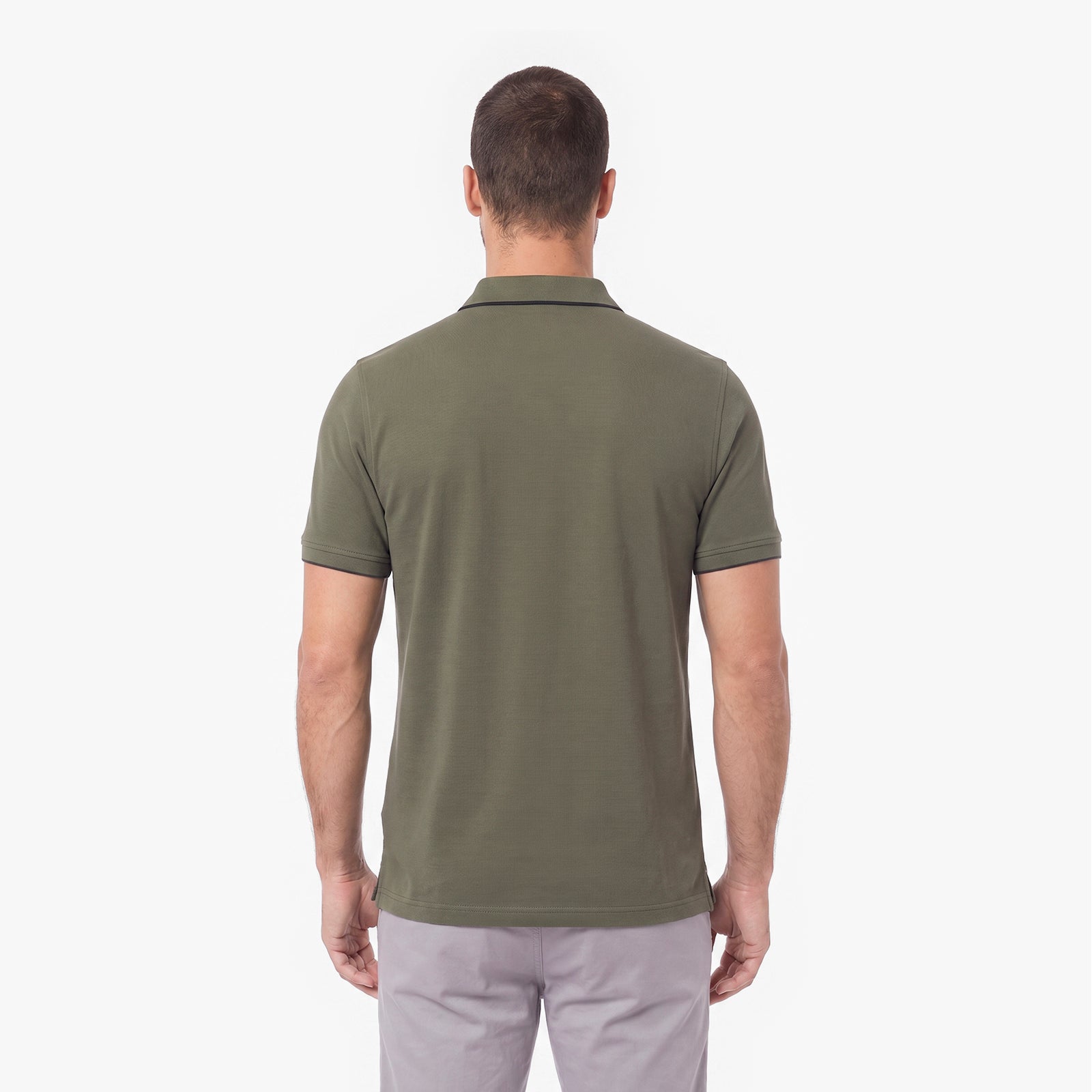 A man viewed from the back wearing an olive green short-sleeve polo shirt and light gray trousers